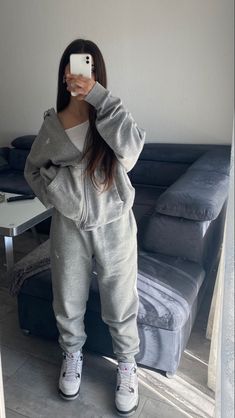 a woman taking a selfie in front of a couch wearing grey sweatsuits