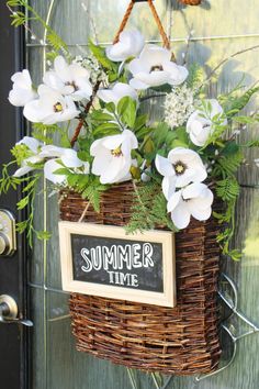 a basket filled with white flowers hanging from the side of a door next to a sign that says summer time