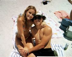 a man and woman are sitting on the beach with their arms around each other, smiling