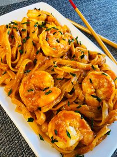 a white plate topped with pasta and shrimp next to chopsticks on a table