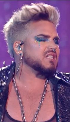 a man with blonde hair and piercings on his ear wearing silver jewelry, standing in front of a purple background