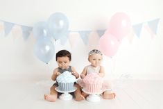 two babies sitting next to each other with cupcakes and balloons in the background