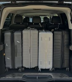 four suitcases are stacked in the back of a van with its doors open and seats folded down