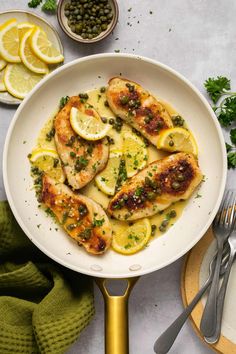 a white plate topped with chicken covered in lemons and capers next to olives