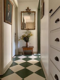 a hallway with green and white checkered flooring next to a wooden bench in front of a mirror