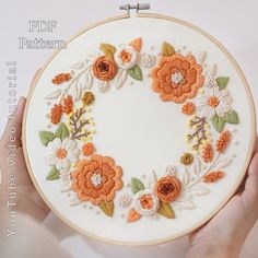 a hand holding a white embroidery hoop with orange flowers on it