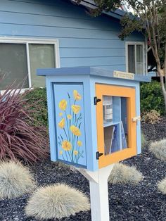 a blue and yellow mailbox with flowers painted on it's side in front of a house