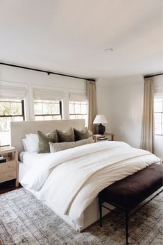 a large bed sitting in the middle of a bedroom next to two lamps and windows