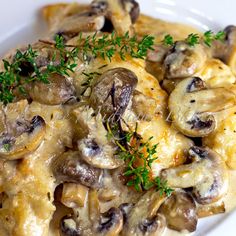 a white plate topped with pasta covered in mushrooms and cheese sauce, garnished with parsley