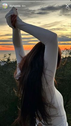 a woman in white shirt doing yoga on top of a hill at sunset with her arms stretched out