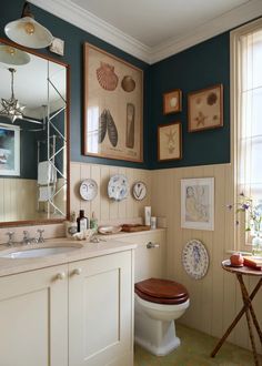 a bathroom with blue walls and pictures on the wall above the toilet, along with other decor