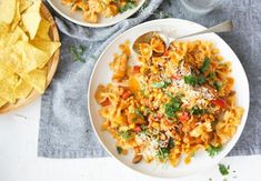 two plates of pasta and tortilla chips on a table