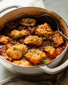 a pot filled with meatballs and sauce on top of a table next to a spoon