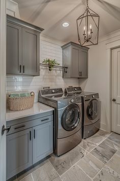 a washer and dryer in a laundry room with gray cabinetry, light fixture, and tile floor