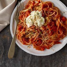 a white plate topped with pasta and sauce next to a silver fork on top of a table