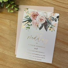 a wedding card with flowers on it sitting next to a flower pot and greenery