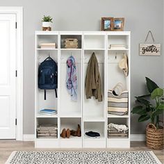 a white bookcase filled with clothes next to a rug and potted plant on top of a hard wood floor