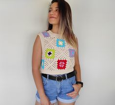 a woman standing in front of a white wall wearing shorts and a crochet top