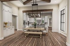 an open concept kitchen and dining room with wood flooring, white cabinets and wooden beams