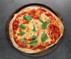 a pizza with basil leaves on it sitting on top of a pan covered in cheese