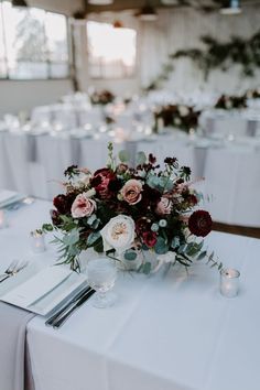 the centerpieces on this table are filled with red and white flowers, greenery, and candles