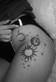 a woman laying on top of a bed with tattoos on her thigh and the sun and moon