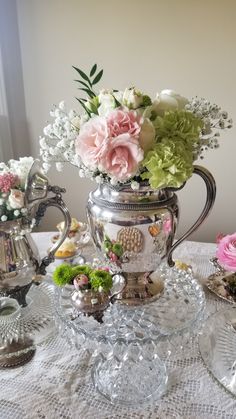 a silver tea pot filled with flowers on top of a white tablecloth covered table