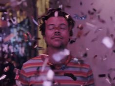 a man with his eyes closed standing in front of confetti falling from the ceiling