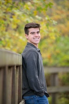 a young man standing on a bridge in front of trees and bushes, smiling at the camera