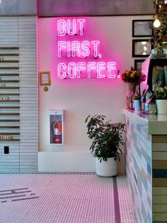 a pink neon sign that says but first, coffee on the wall next to a potted plant