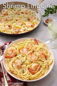 two plates of shrimp linguine on a marble table with wine glasses and utensils