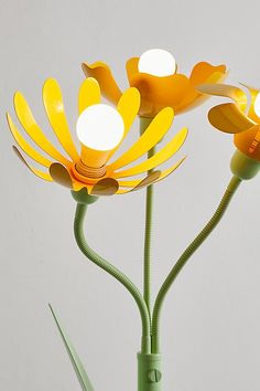 two yellow flowers in a green vase on a white surface with one flower turned upside down