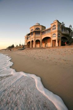 a large building sitting on top of a sandy beach next to the ocean with waves coming in