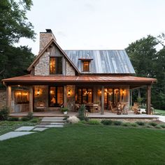 a house that has a metal roof and stone pillars on the front porch with lights on