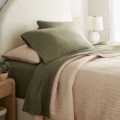 a bed with green sheets and pillows in a bedroom next to a lamp on a nightstand