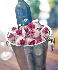 a metal bucket filled with ice and roses next to a bottle of wine on top of a wooden table