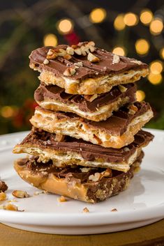 a white plate topped with chocolate covered pretzels and nutty crackers next to a christmas tree