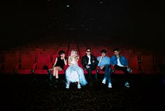 group of people sitting on red chairs in an empty theater with one person holding a cell phone