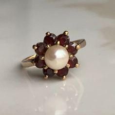 A vintage 9 carat gold Garnet and Pearl ring. CONDITION: Wear consistent with age and use. Stones and Pearl in great condition. Please see photos for more detail. HALLMARKED 9 CARAT GOLD, ASSAYED IN LONDON 1976 GARNET SIZE: 3mm (0.10 carats) PEARL SIZE: 6mm SETTING DIAMETER: 13mm BAND WIDTH (NARROWEST): 1.5mm RING SIZE: UK: M | US: 6 WEIGHT: 4.0 grams (HZ)