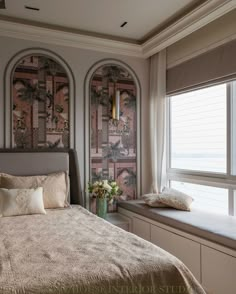 a bed sitting next to a window in a bedroom under two arched windows with palm trees on them