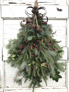 a christmas wreath hanging on the side of a white door with pine cones and berries