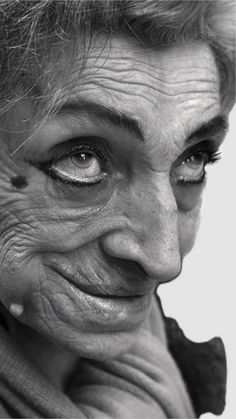 black and white photograph of an old woman with wrinkles on her eyes looking at the camera