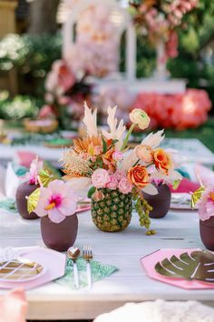 a table set with pineapples, flowers and other decorations for an outdoor party