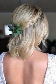 the back of a woman's head wearing a white top and green flowers in her hair