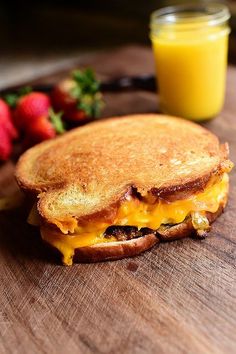 a grilled cheese sandwich sitting on top of a wooden cutting board next to strawberries