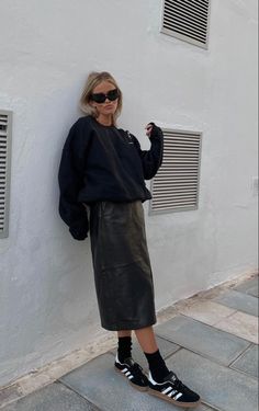 a woman leaning against a wall with her hand on her hip and wearing black sneakers