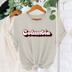 a white shirt with the word columbia printed on it and a green plant behind it