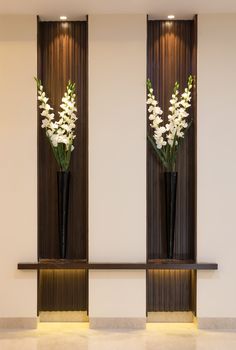 two tall black vases with white flowers in them sitting on a shelf next to each other