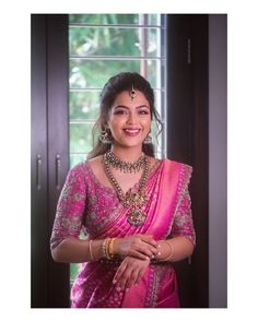 a woman in a pink sari smiling for the camera with her hands folded out