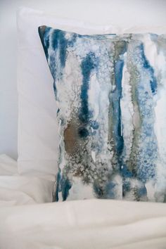 a blue and white pillow sitting on top of a bed next to a white comforter